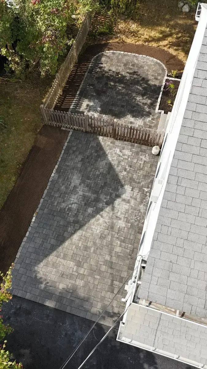 Overhead view of a concrete patio next to a yard enclosed by a fence and a rooftop.