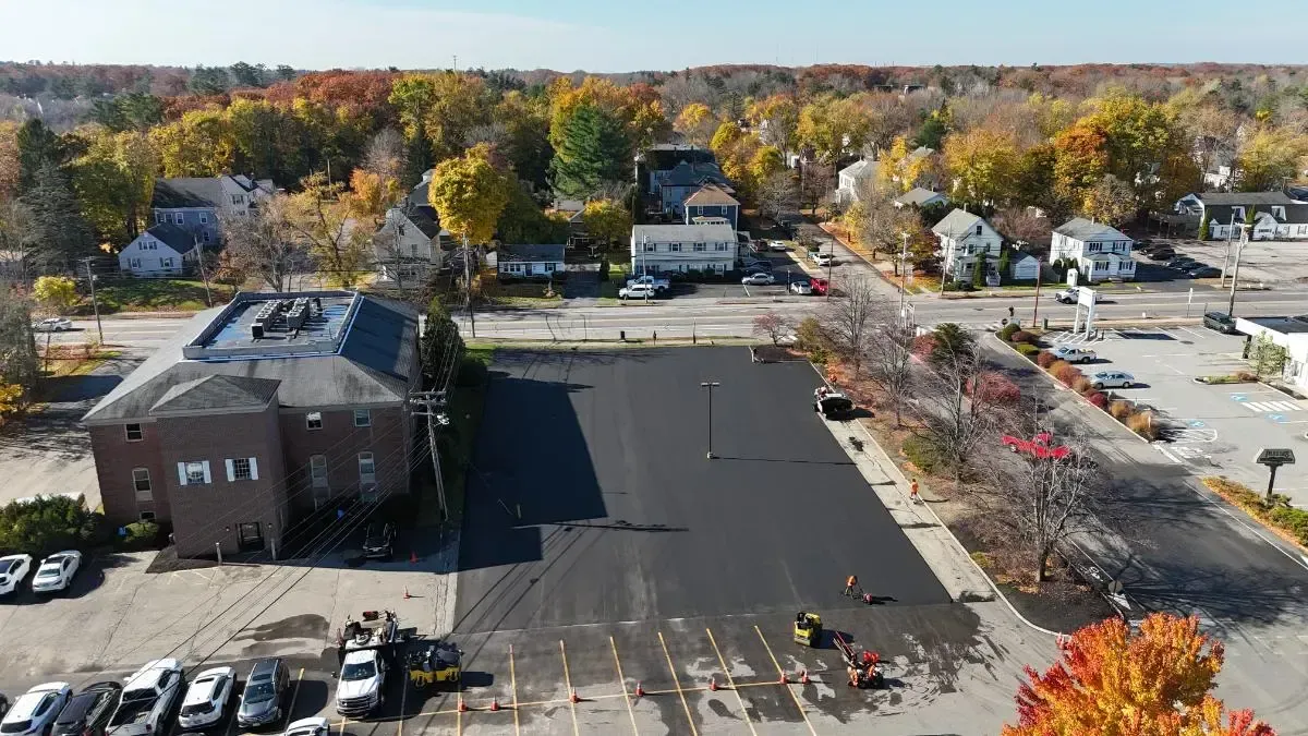 Newly paved parking lot with workers and nearby buildings under a blue sky in autumn.
