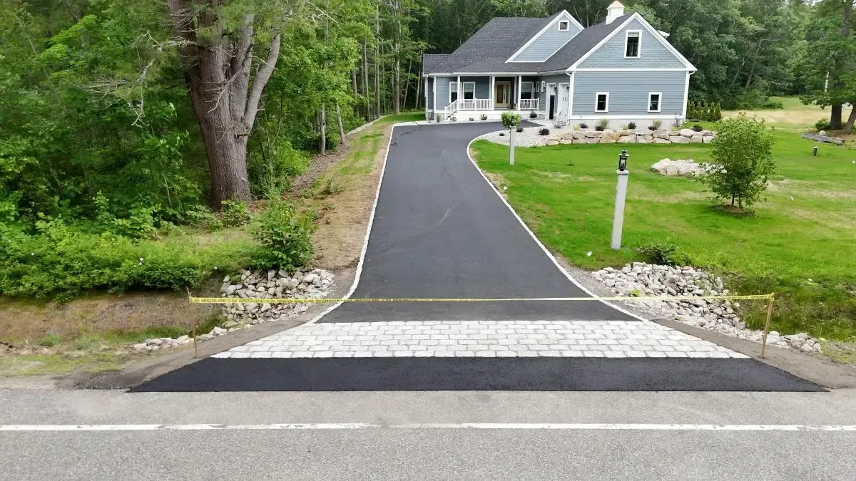Asphalt driveway leading to a blue house on a green lawn. Stone border.