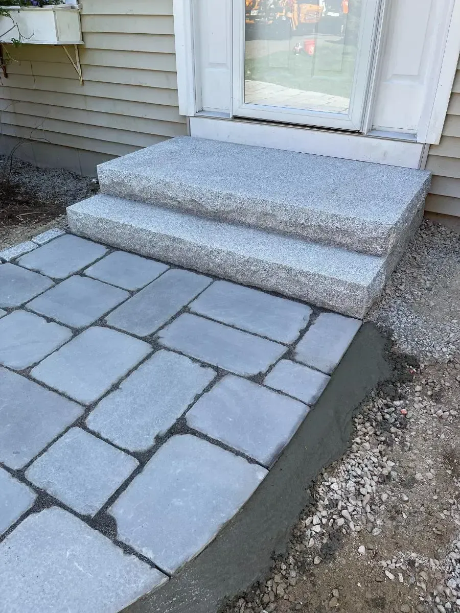 Stone steps leading to a door, with gray pavers and gravel in front.
