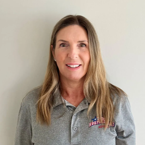 Woman with long blonde hair smiles, wearing a gray polo shirt with 