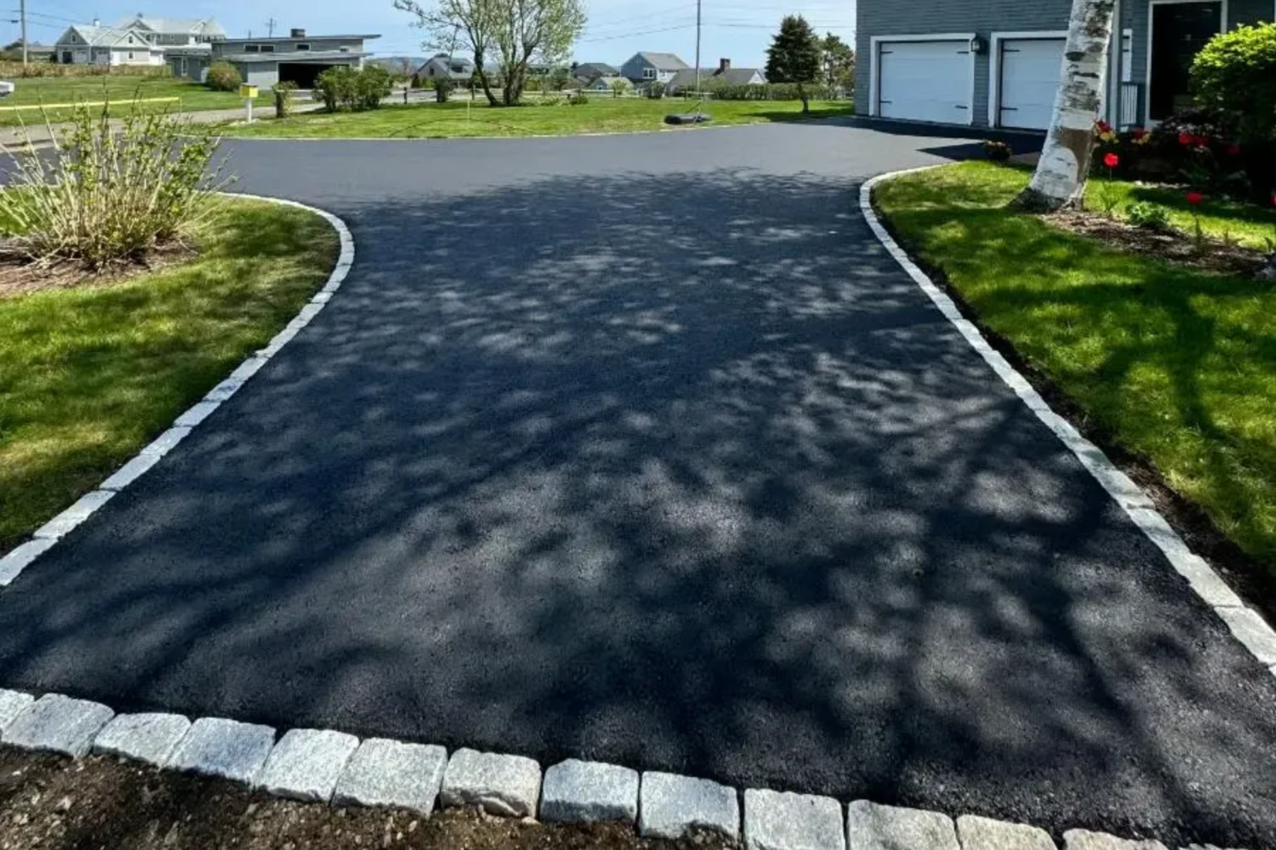 Black asphalt driveway with light-colored border, leading to a garage. Green grass surrounds.