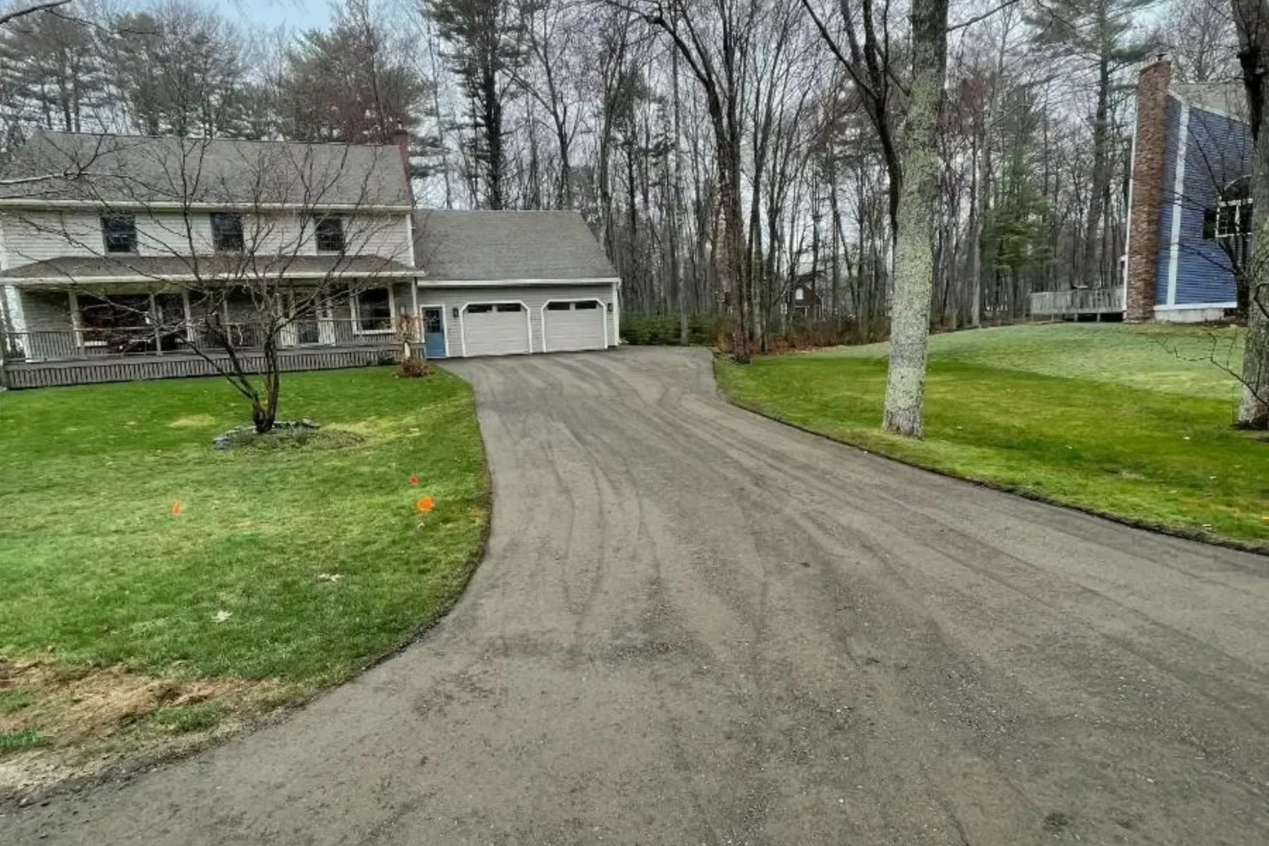 Two-story house with a gravel driveway and attached garage; grassy yard, trees in background.