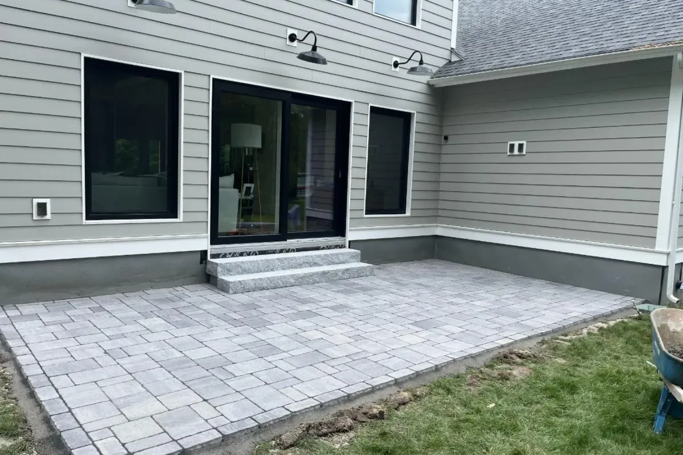 Gray paver patio outside a house with sliding glass door and steps.