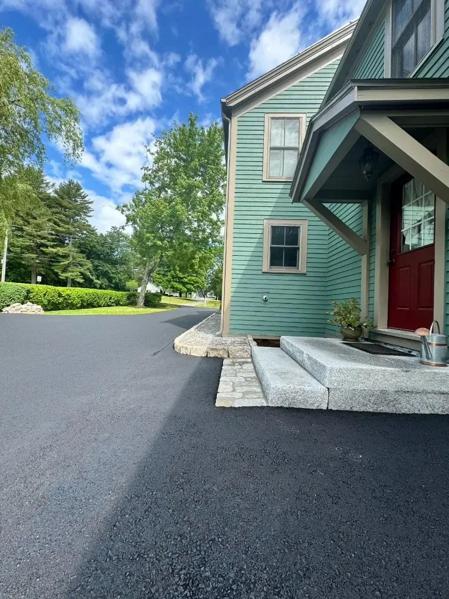 A teal house with a red door, a black driveway, and a blue sky.