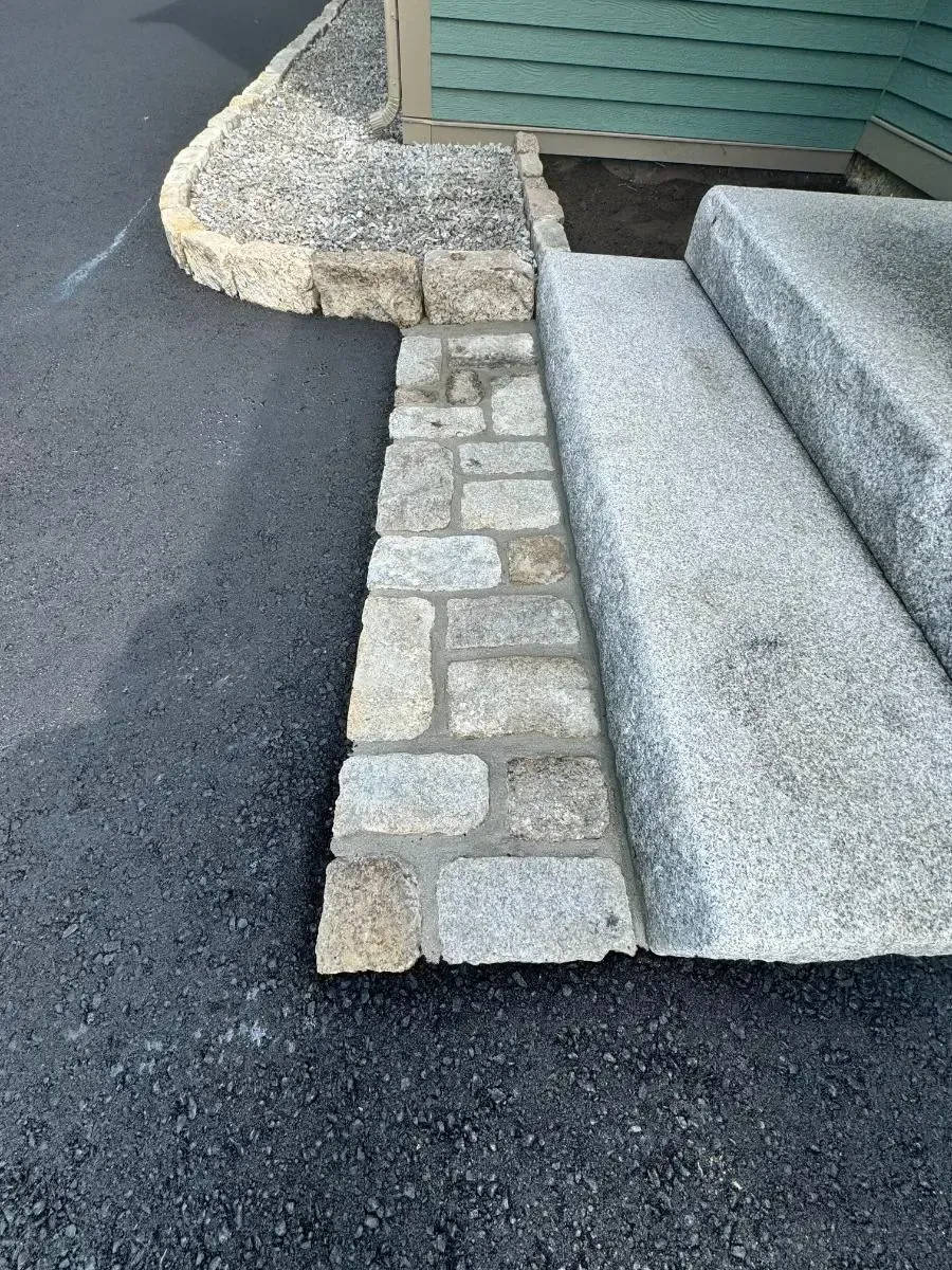 Stone steps and ramp with a brick border next to an asphalt driveway.