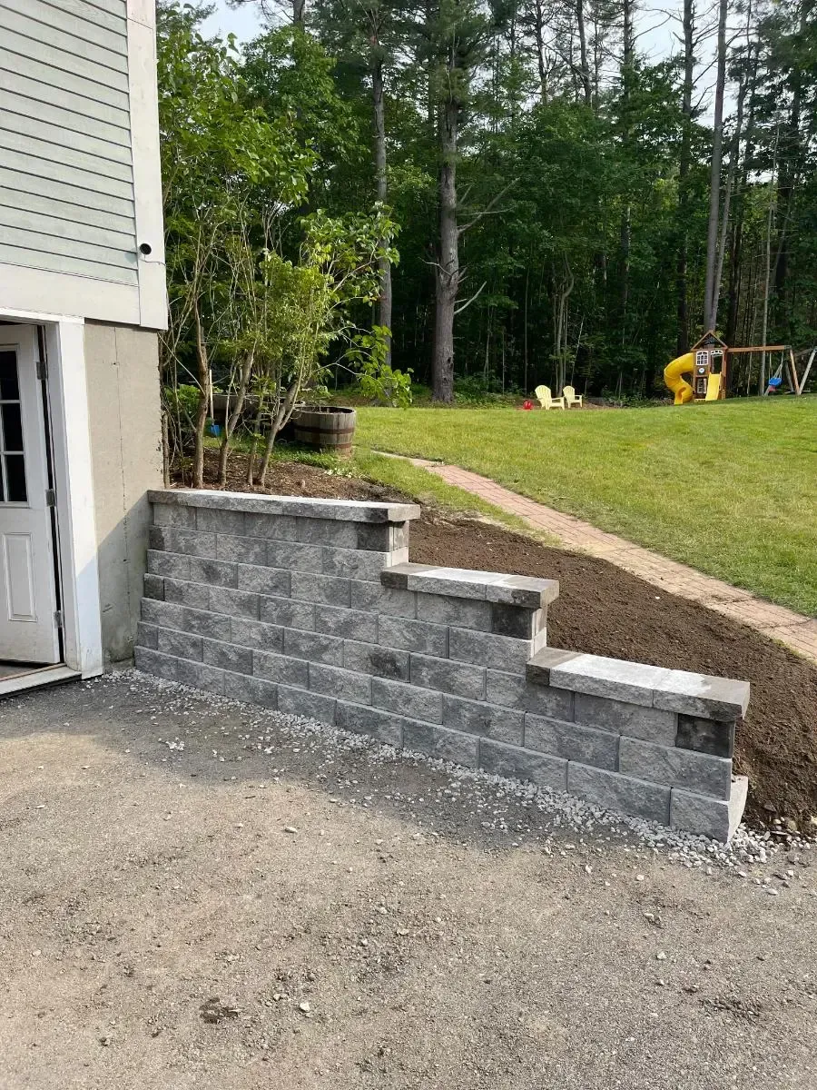 Stone retaining wall with steps leading to a yard, next to a building.