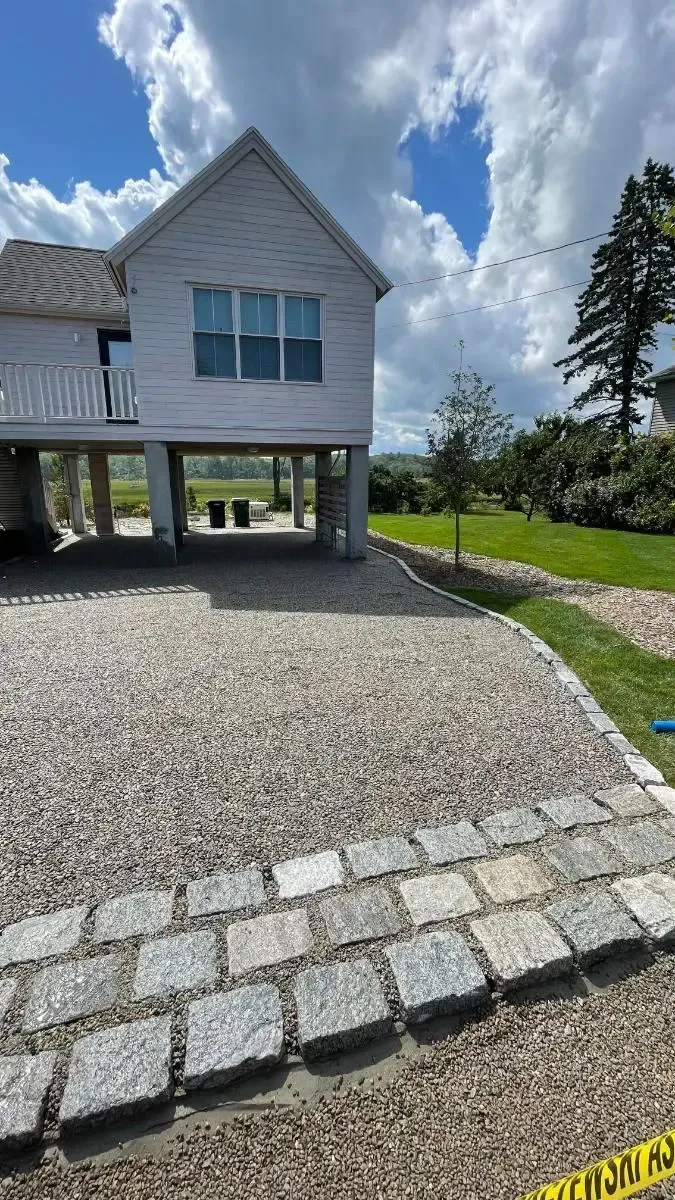 House with gravel driveway and stone border, on a sunny day.
