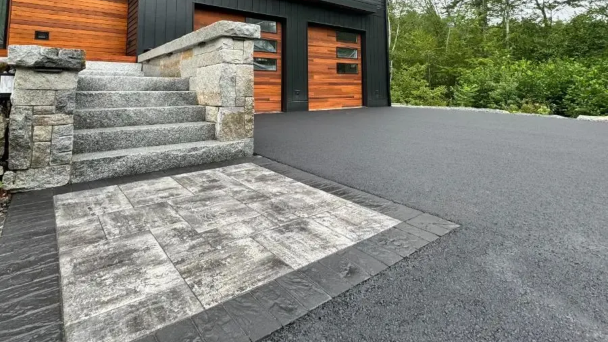 Exterior view of a modern house with a paved driveway, stone steps, and wooden garage doors.