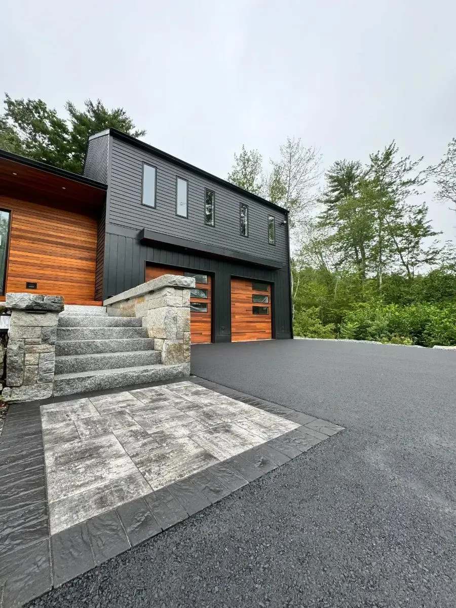 Modern house with black siding, wood garage doors, stone steps, and dark driveway.