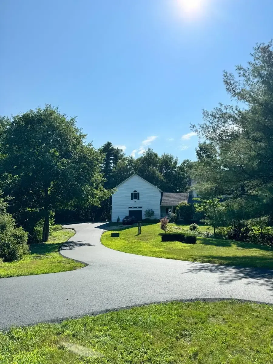 Paved driveway leading to a light-blue house with multiple garage doors, under a clear, blue sky.