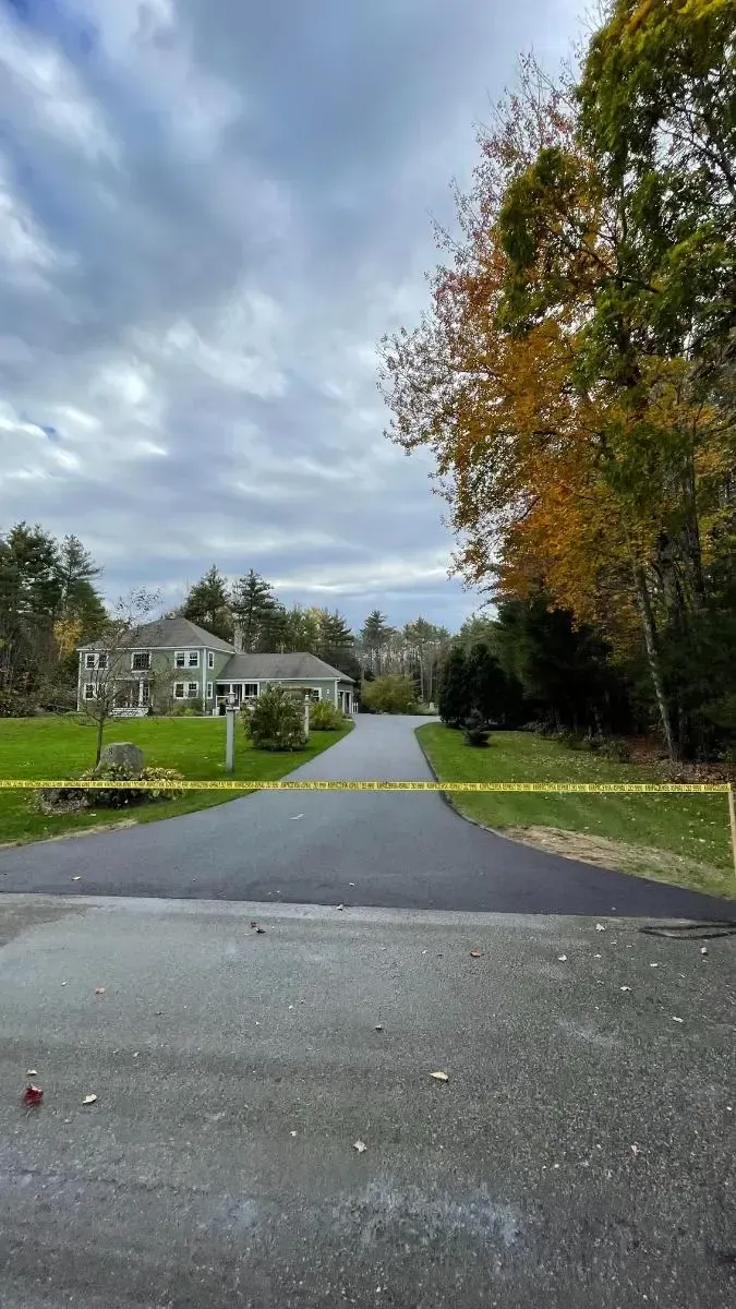 House with teal siding, dark driveway, and green lawn under a blue sky, framed by trees.