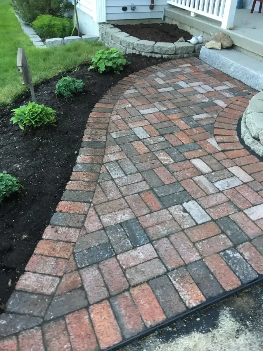 Brick pathway leading to a doorway, bordered by dark mulch and plants.