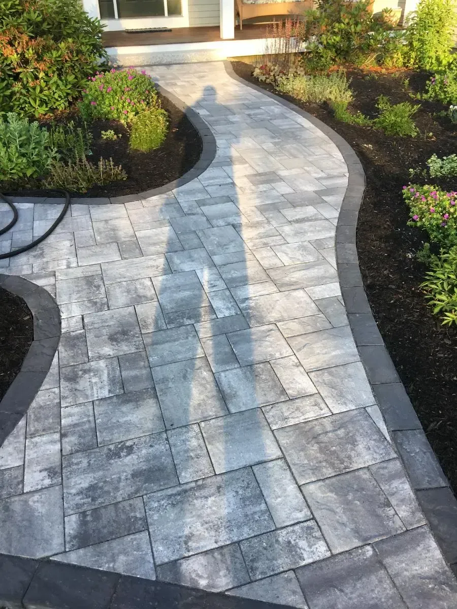 Stone paver walkway with dark border, curves through landscaped garden.