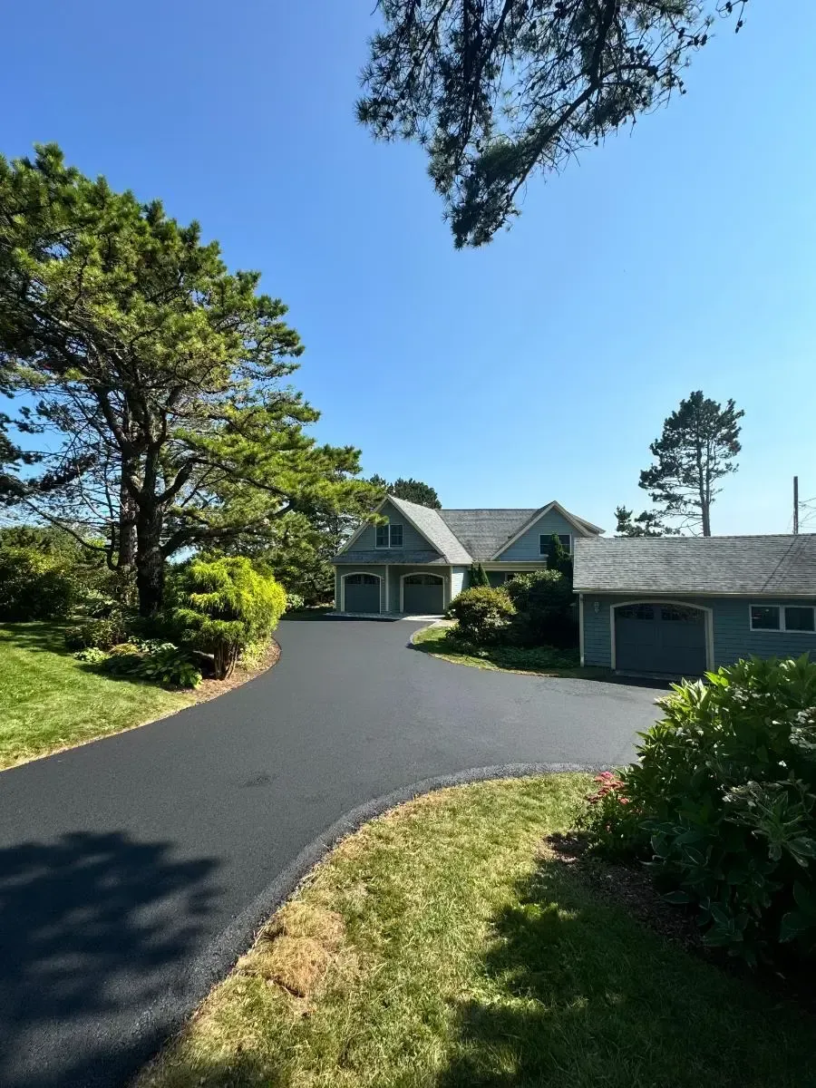Paved driveway leading to a light-blue house with multiple garage doors, under a clear, blue sky.