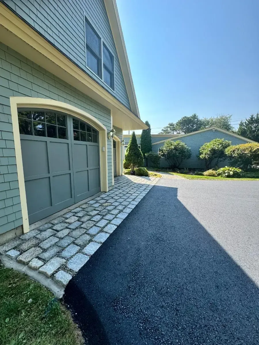 Cobblestone walkway curves toward a gray house on a sunny day.