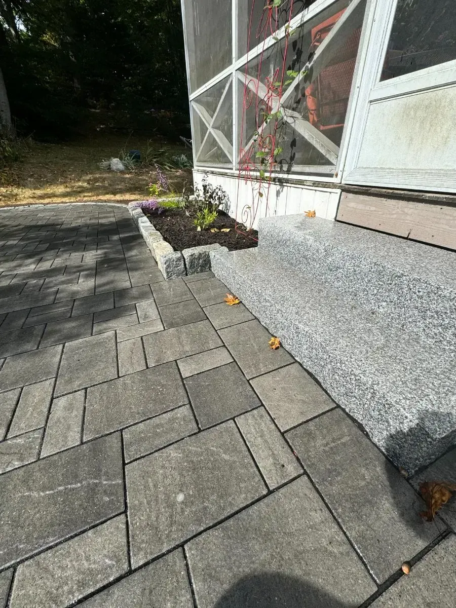 Gray pavers lead to a porch with a flower bed on the side.