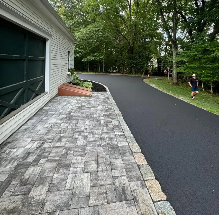 Driveway of asphalt and pavers with a person running nearby. Trees surround.