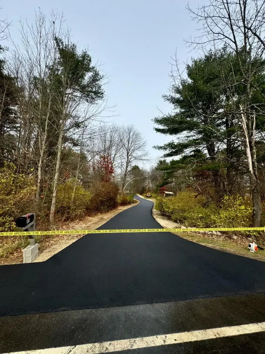 House with teal siding, dark driveway, and green lawn under a blue sky, framed by trees.