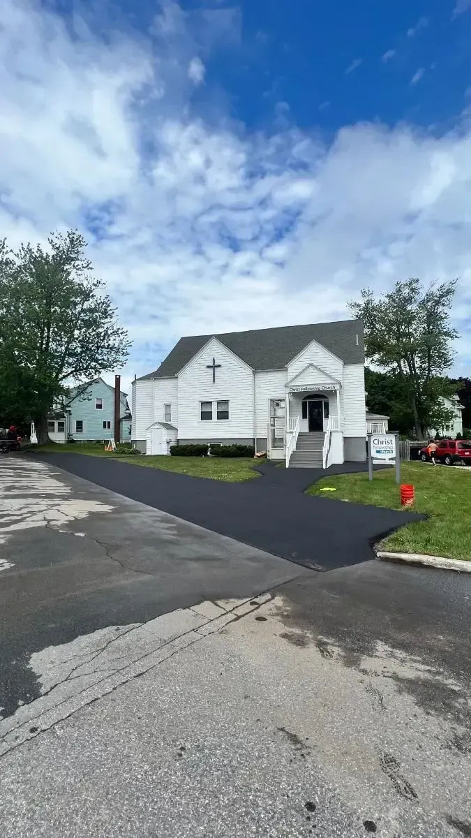White church with a cross on the front, set on a newly paved road on a cloudy day.