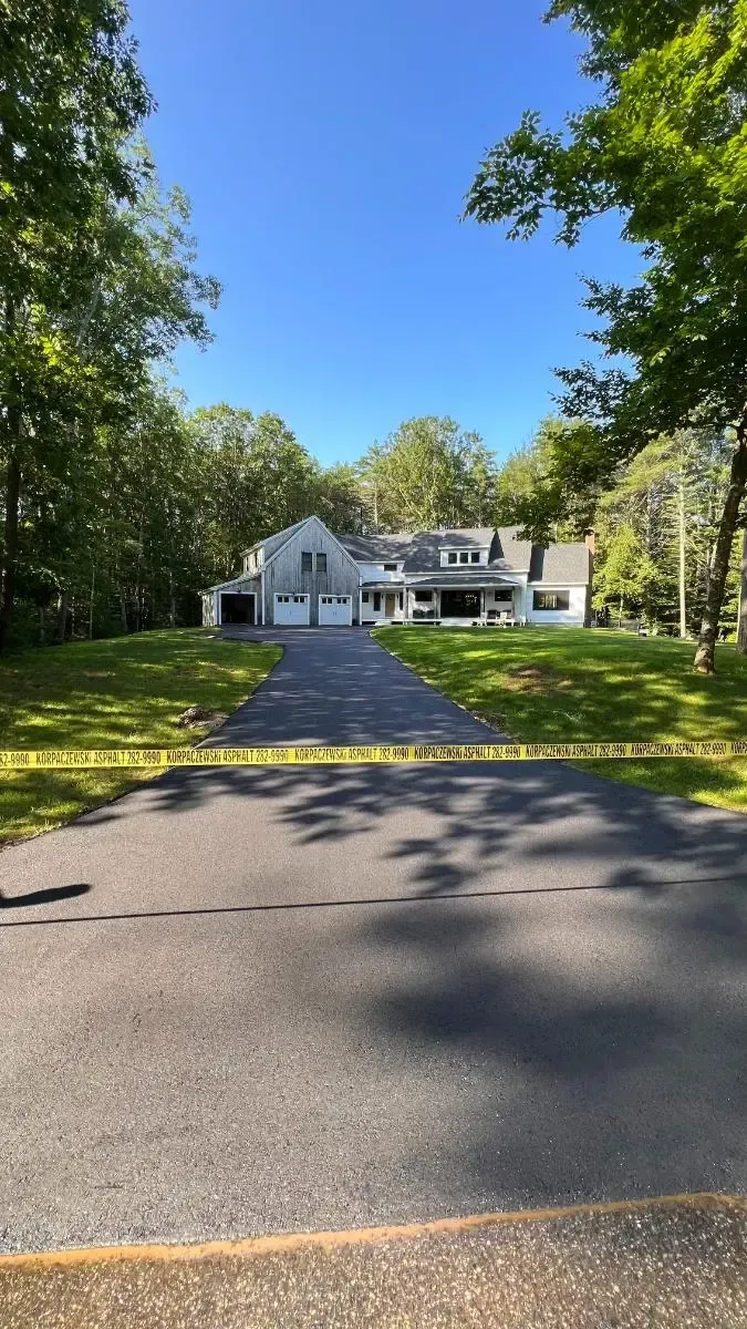Two-story gray house with white trim, three-car garage, long asphalt driveway, set among trees and green lawn.