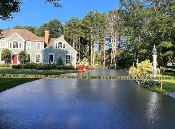 A two-story gray house with a freshly paved black driveway and a small lighthouse ornament.
