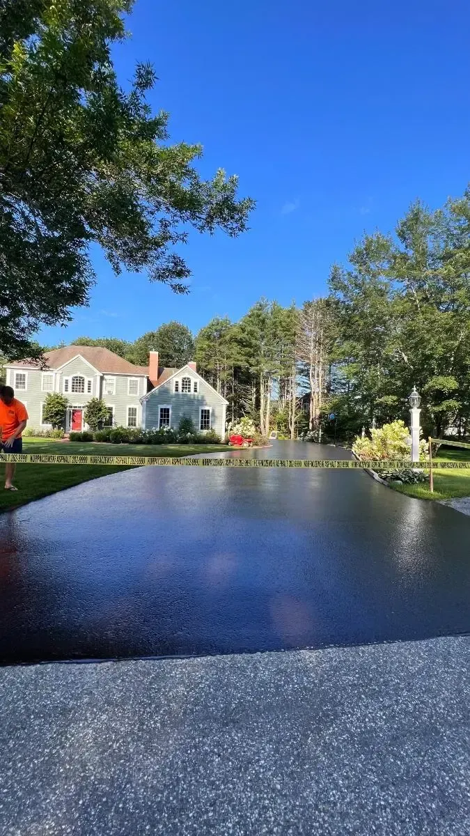 Newly paved driveway leading to houses with blue sky and trees.
