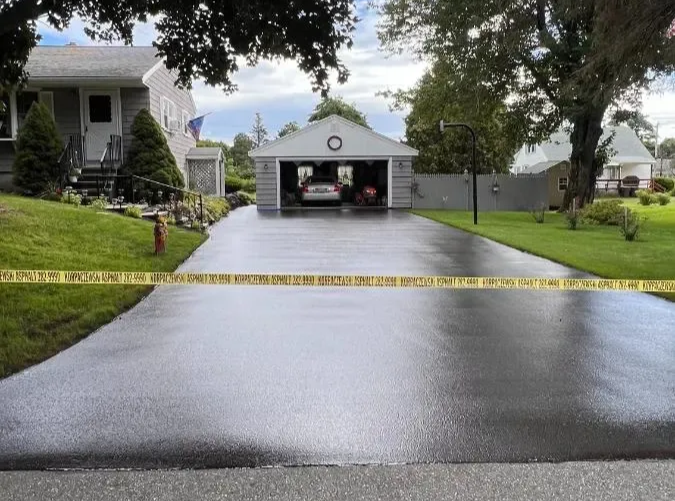 Black asphalt driveway blocked by yellow caution tape; house and garage in background.