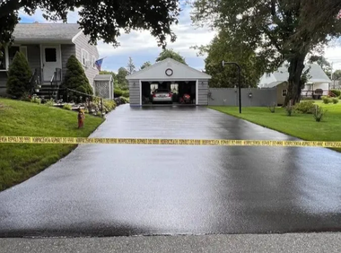 Black asphalt driveway blocked by yellow caution tape; house and garage in background.