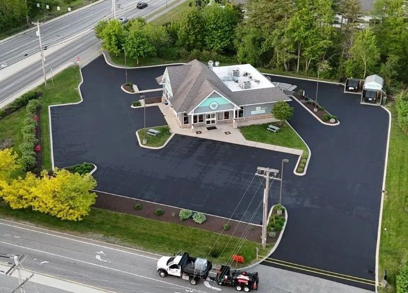 Aerial view of a building with fresh asphalt, surrounded by landscaping and a service truck.