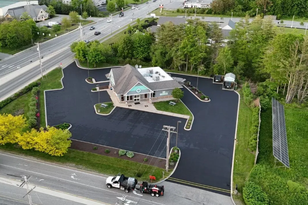 Aerial view of a paved parking lot surrounding a teal building, with a truck and trailer in the foreground.