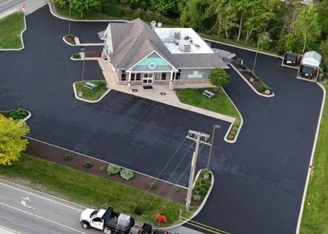 An aerial view of a building with a newly paved parking lot. A white truck is visible on a road in the foreground.