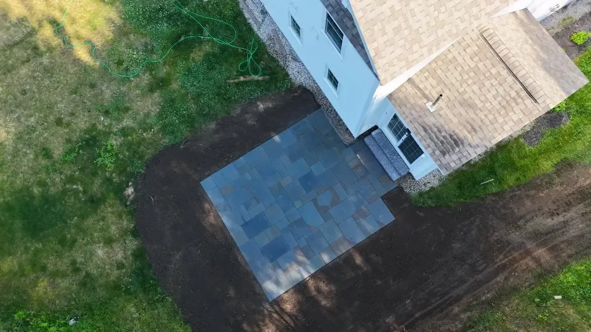 Overhead view of a house with a newly constructed dark stone patio surrounded by grass and dirt.