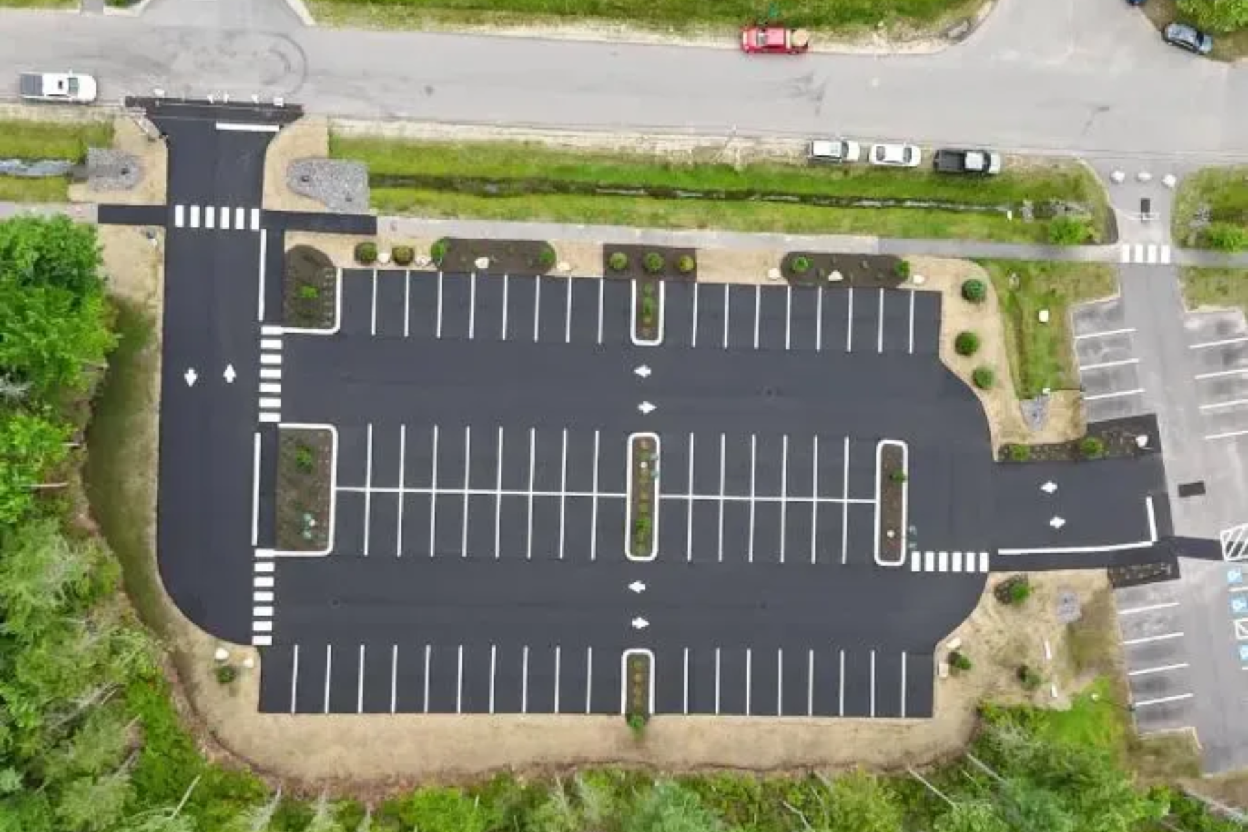Aerial view of a paved parking lot with marked spaces, landscaping, and pedestrian crosswalks.