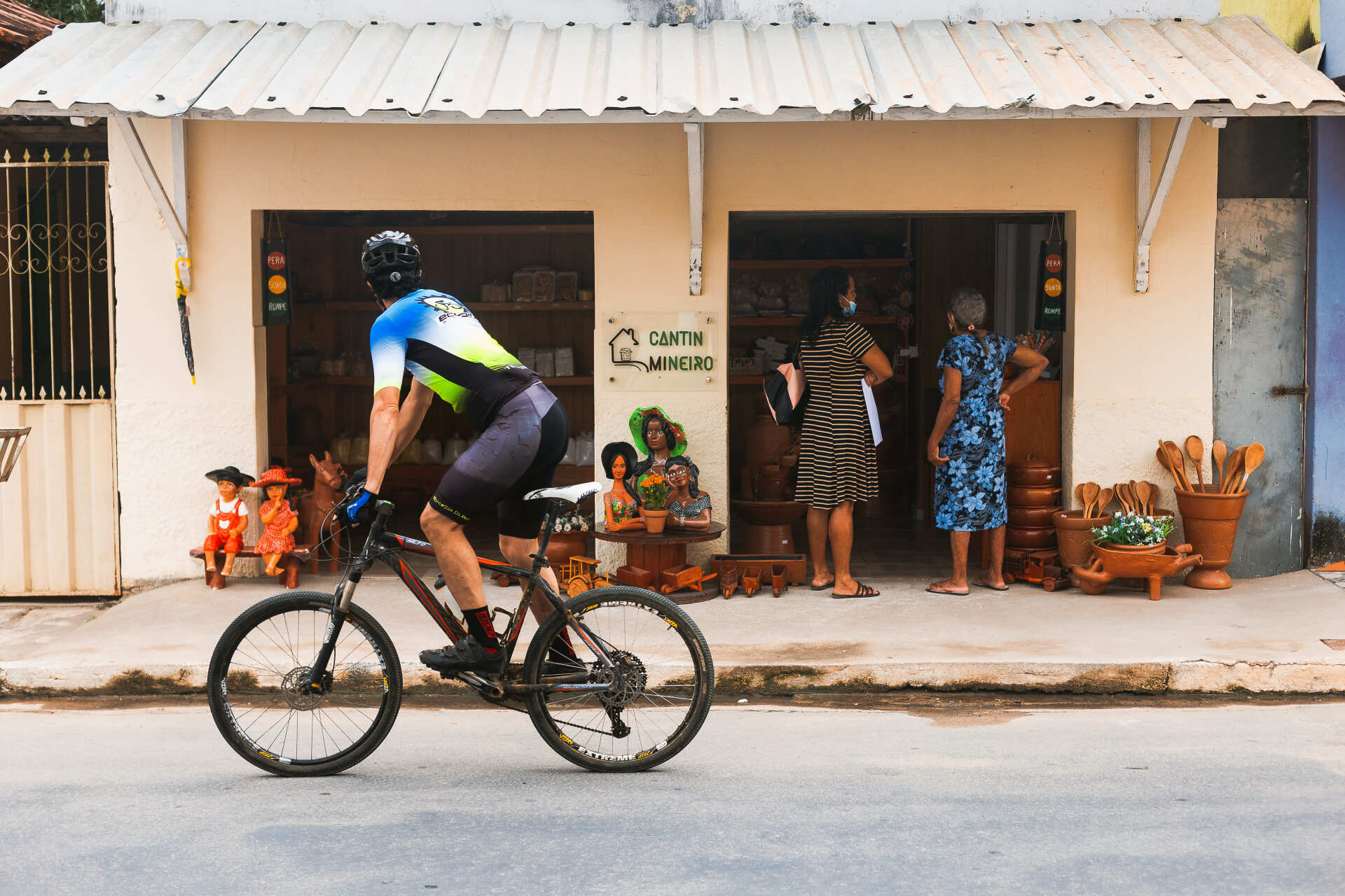 Um homem está andando de bicicleta pela rua em frente a uma loja.