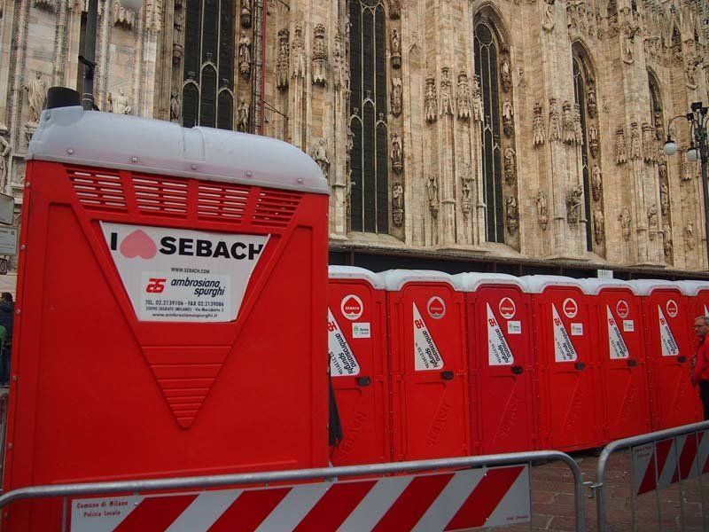 Fila di bagni chimici rossi di fronte a un edificio con pietra lavorata.
