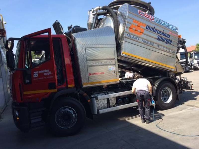 Autospurgo rossa e argento; un operaio si occupa del veicolo all'esterno.