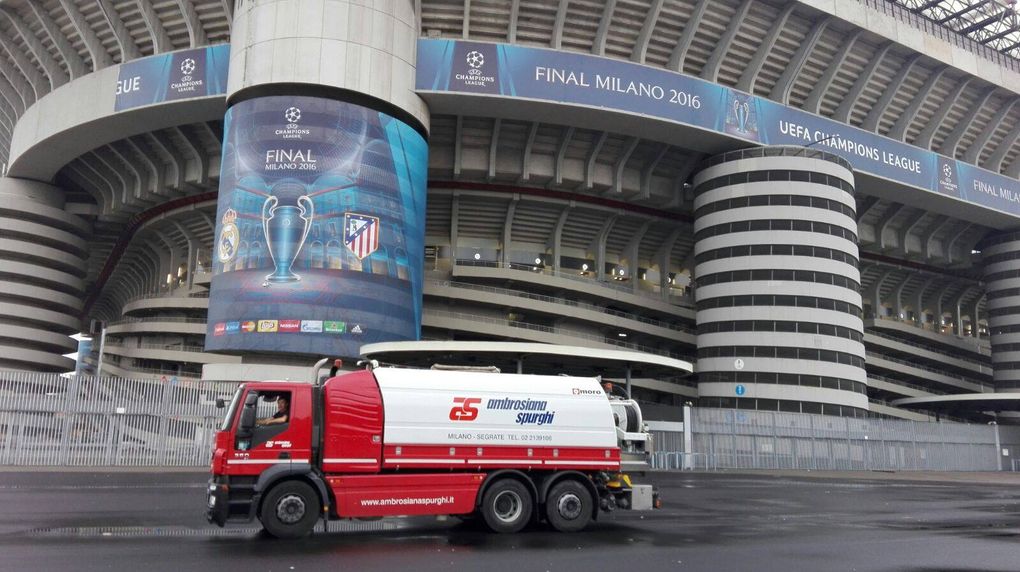 Un camion rosso per l'acqua davanti a un grande stadio con striscioni per la finale di Champions League.