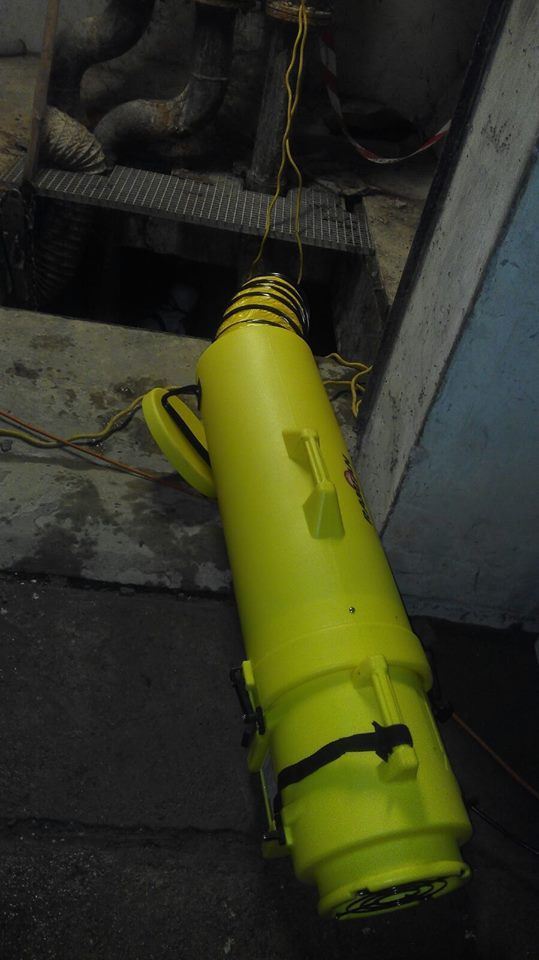 Dispositivo cilindrico giallo sospeso in un ambiente industriale buio.