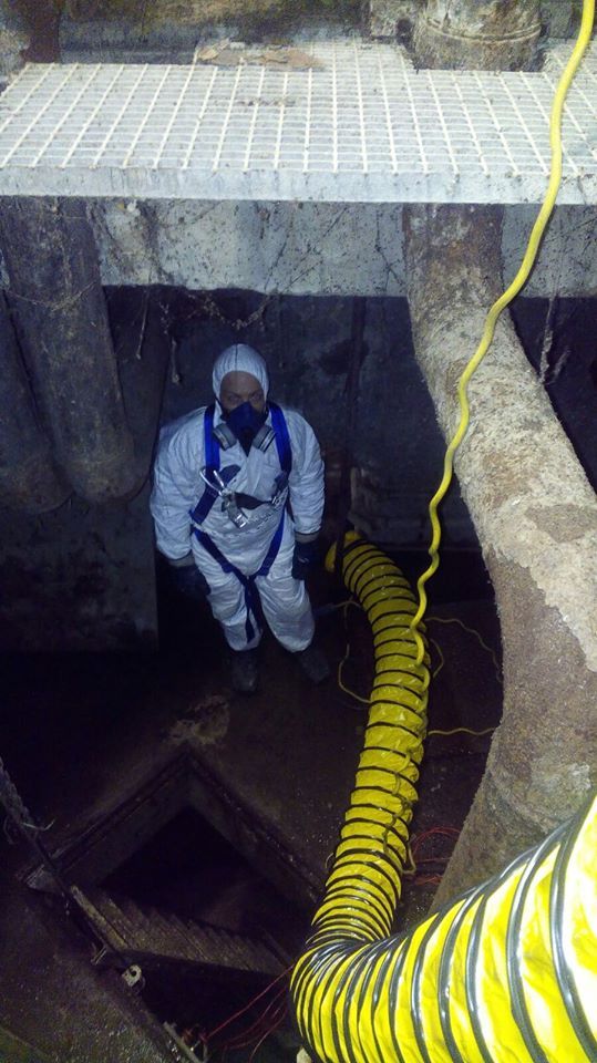 Persona con tuta protettiva in uno spazio confinato, tubo di ventilazione giallo.