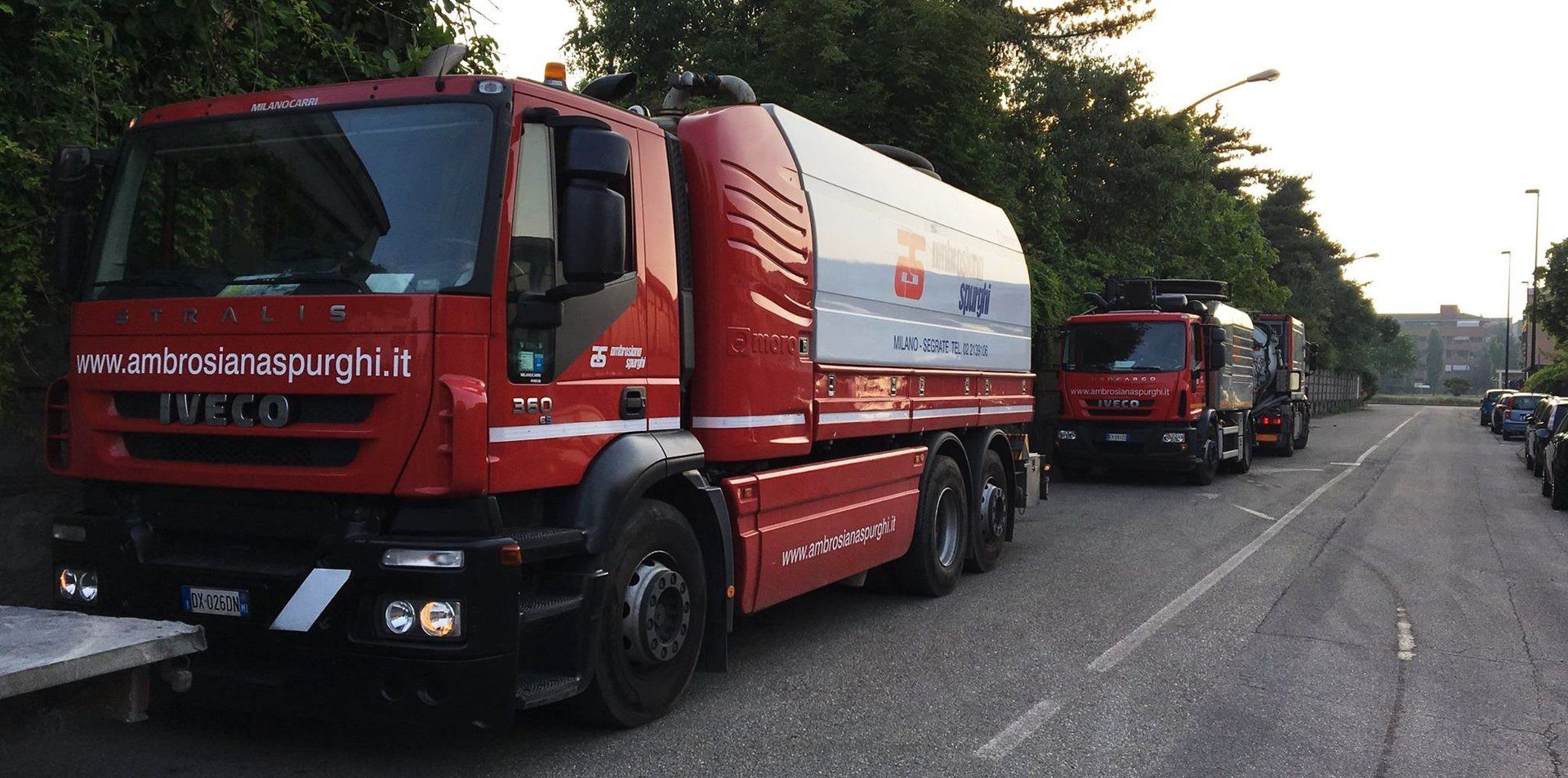 Camion rossi parcheggiati su una strada asfaltata accanto a una fila di alberi.