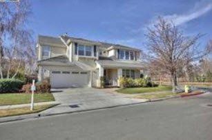 Two-story beige house with white garage door and driveway, blue sky, tree in yard, and sidewalk. Pleasanton CA Realtor Gina Bentley
