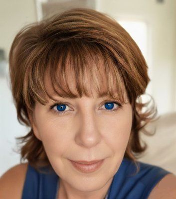 Woman with blue eyes and short brown hair, smiling, wearing a blue top, indoors.