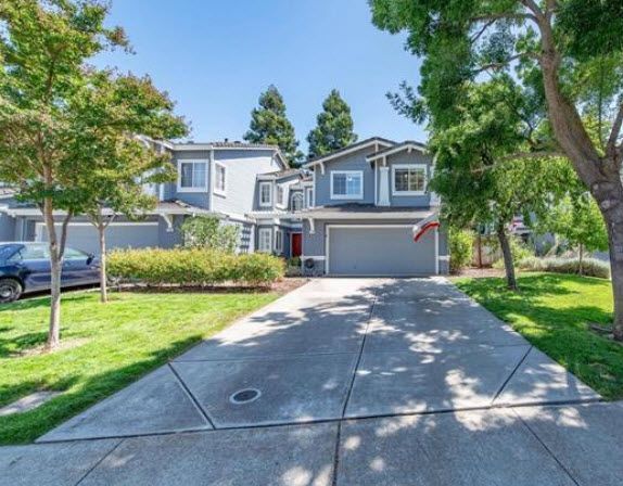 Blue two-story Townhouse with gray garage and driveway, green lawn, trees, and blue sky. Livermore Realtor Gina Bentley