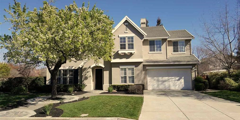Two-story beige house with a blossoming tree in the front yard, blue sky above in Livermore CA Represented Seller