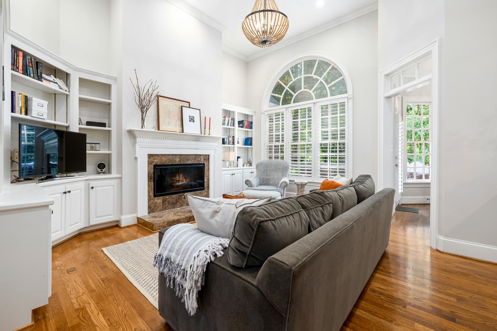 Living room with fireplace, built-in shelving, arched window, and a gray sofa.