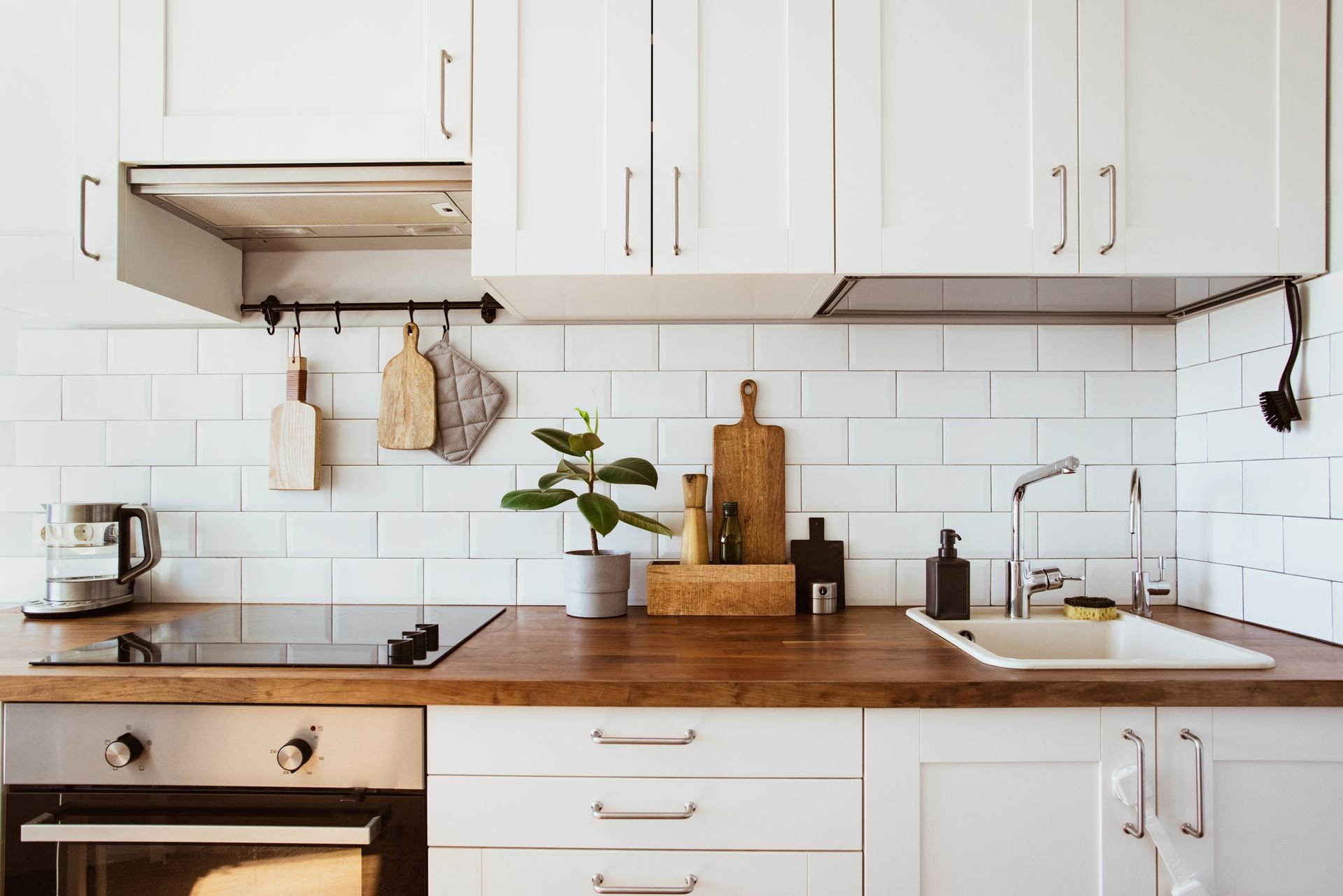 A kitchen with white cabinets , a stove , a sink , and a potted plant on the counter.