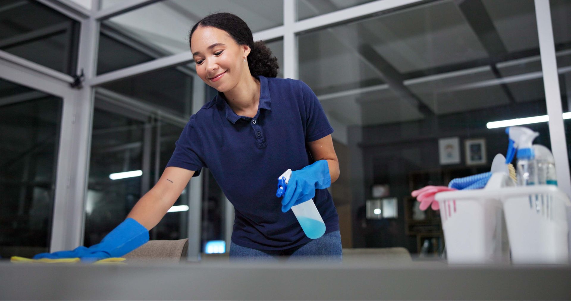 Female worker spraying and wiping desk in clean office space