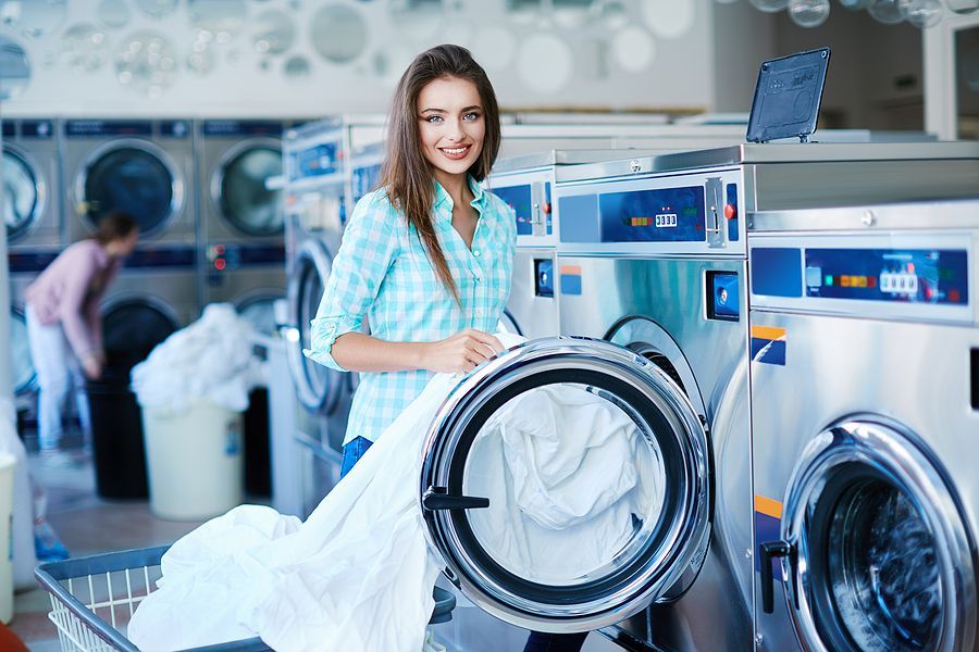 A woman is standing in front of a washing machine in a laundromat.