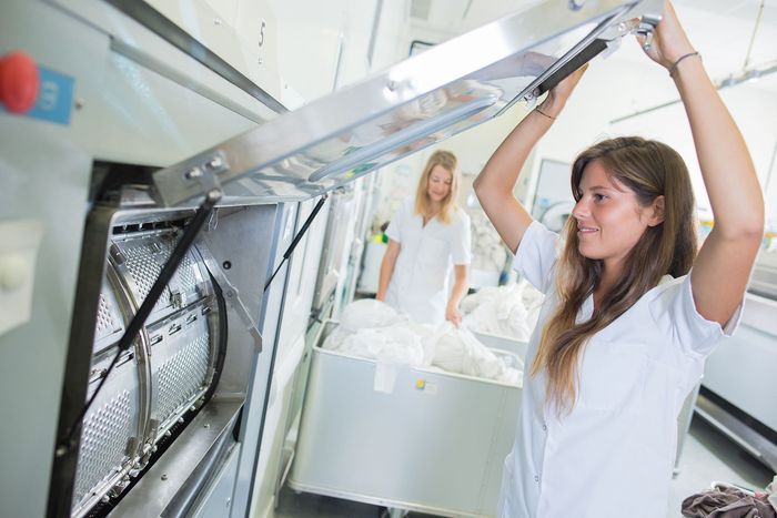 Two women are working in a laundromat and one is lifting something up